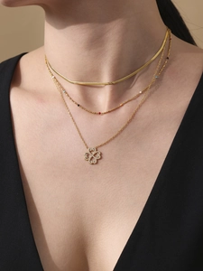 Detail of layered gold necklaces with snake chain and diamond-studded clover pendant