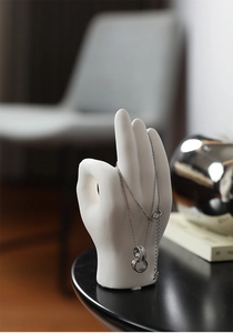 Close-up of silver-tone double ring necklace hanging on a white ceramic hand sculpture