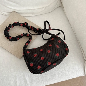 Corduroy shoulder bag with strawberry print and ruched strap on a white sofa