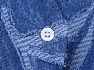 Close-up of blue denim jacquard fabric texture with fringe detail and a white button