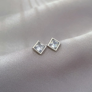 Macro shot of silver square cubic zirconia stud earring on smooth satin fabric