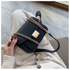 Detail of a black faux leather crossbody bag featuring a golden lock and chain strap