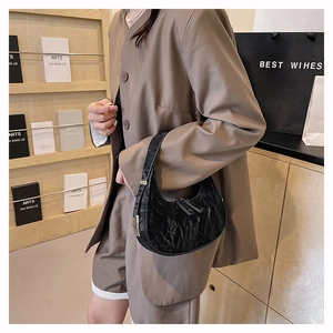 Close-up of black wrinkled crescent bag styled with a brown blazer and silver hardware