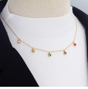 Detail of gold necklace with five colorful round rhinestones on a white turtleneck