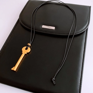 Close-up of golden key pendant on black leather case with a cord chain detail