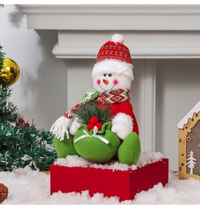 Detail of plush Christmas snowman ornament wearing red knit hat and holding a festive gift bag