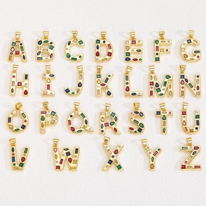 Golden alphabet pendants A-Z with colorful zircon stones on a white background