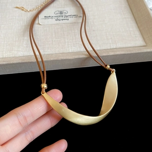 Macro shot of minimalist gold irregular metal pendant with matte brushed finish and brown cord