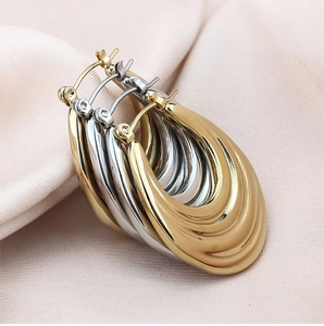 Detail of tear-drop metal earrings in gold and silver finish on soft pink silk fabric