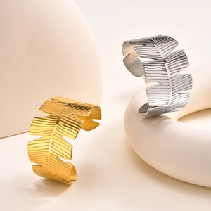 Elegant gold and silver leaf-shaped stainless steel open cuff bracelets on marble stands