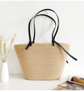 Detailed shot of a beige woven tote bag with black knotted straps on a minimalist desk