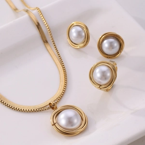 Macro shot of gold-tone mesh chain necklace, stud earrings and pearl ring set on white