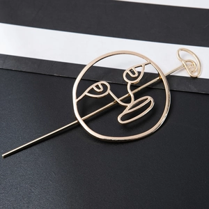 Detail of golden metal hair stick featuring abstract facial line art in a circular frame