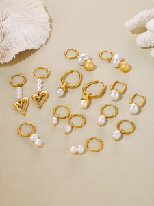 Flat lay of multiple 18k gold plated pearl earrings on a beige textured stone base