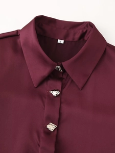 Detalle de camisa satinada color burdeos con botones plateados irregulares y textura de seda