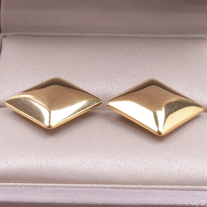 Macro shot of gold-plated square pyramid stud earrings on silk jewelry box lining