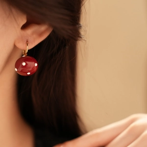 Close-up of red and white polka dot enamel ball earring worn on ear with gold metal hook