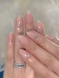 Detail of long almond nails with nude pink base, silver glitter gradient and rhinestones