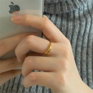 Detail of twisted knot gold ring shown on hand with a soft textured background