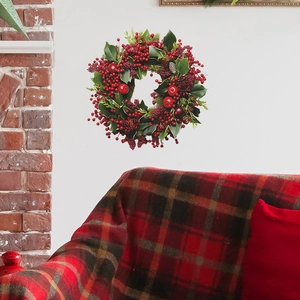 Couronne de Noël avec baies et pommes de pin sur mur blanc au-dessus d'un canapé rouge