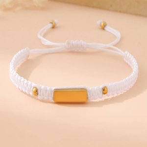 Macro shot of white woven bracelet with a polished gold rectangular metal plate