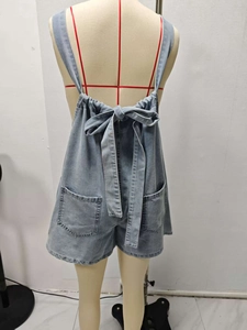 Detail of light blue denim romper featuring adjustable back bow tie and dual rear pockets