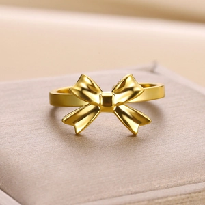 Close-up of a polished gold bow ring displayed on a textured jewelry gift box