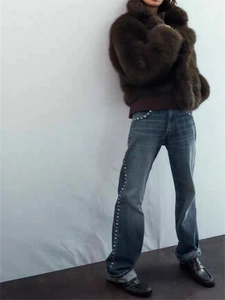 Détail d'un manteau en fausse fourrure et jean perlé sur mannequin devant un mur gris