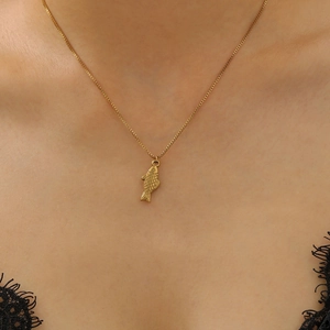 Detailed view of a gold fish pendant on a delicate chain necklace worn by a model