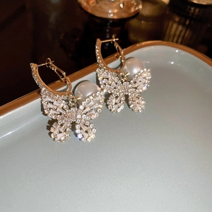 Detail of luxury butterfly drop earrings with shiny crystals and large pearls on a tray