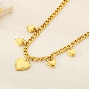 Close-up of golden stainless steel heart necklace with beaded heart pendant on textured background