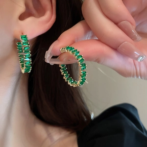 Detail of gold-plated hoop earrings with green zircon stones worn by a model