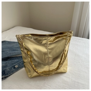 Detailed view of a gold metallic bucket bag with woven chain strap on white bedding