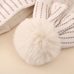 Detailed macro view of the cream knit hat's fluffy faux fur pompom and dotted texture