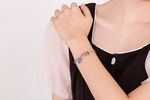 Detail of silver chain bracelet with heart and round charms on a model wrist