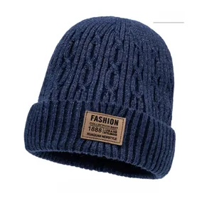 Detail of navy blue cable knit beanie featuring a brown leather patch with fashion text