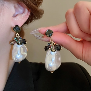 Detailed view of baroque pearl earrings with dark gemstones and golden accents on a model