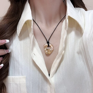 Close-up of gold hollow heart pendant on a black cord necklace worn by a model