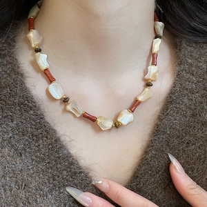 Detailed view of handmade ethnic beaded necklace with shells and red beads on brown sweater