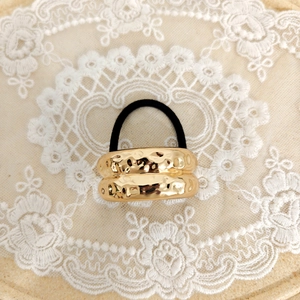 Detail of a minimalist gold hammered metal hair tie with high-elastic black rubber band
