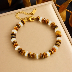 Brown and white beaded bracelet with gold metal accents on a beige display stand