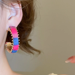 Detail of colorful knitted C-shaped hoop earrings with gold bead trim on model
