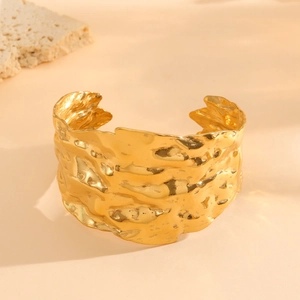 Detail of wide open gold bangle featuring irregular hammered texture and metallic finish