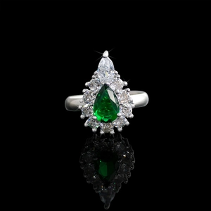Macro shot of teardrop emerald gemstone ring with diamond accents on black surface