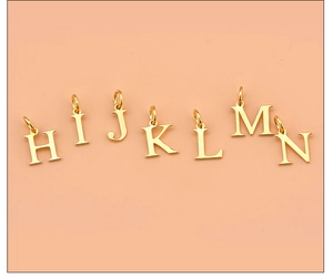 Close-up of golden alphabet charms H to N for DIY necklaces on pink background