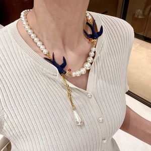 Detail view of a vintage pearl necklace with two blue swallow bird charms on a model