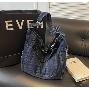 Détail d'un sac cabas en jean bleu foncé avec bords effilochés et texture délavée