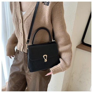 Detail of minimalist black handbag showing gold irregular twist lock and textured PU leather