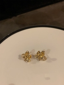 Detailed close-up of golden irregular floral earrings on a white minimalist tray