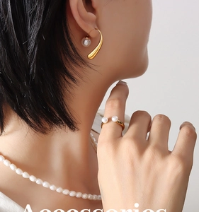 Detail of elegant gold earrings and ring featuring white pearls on a female model